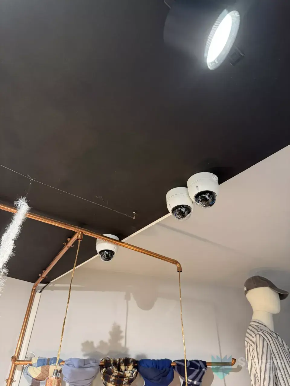 Deux caméras dômes blanches installées au plafond de la surface de vente d'un magasin de prêt-à-porter à Brignoles
