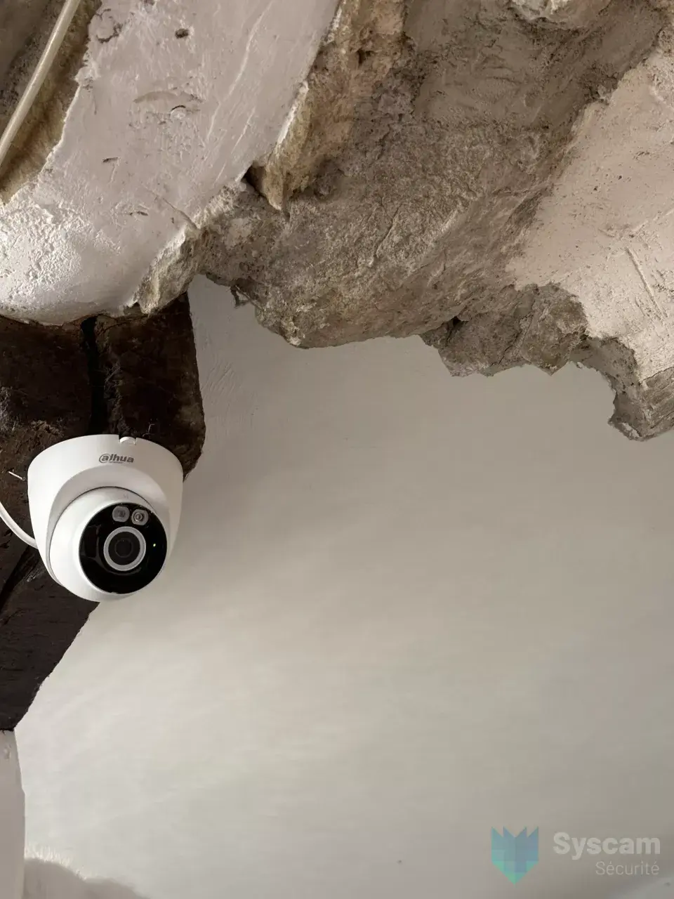 Caméra dôme Dahua fixée sur une poutre ancienne de la réserve, entre pierre et plâtre
