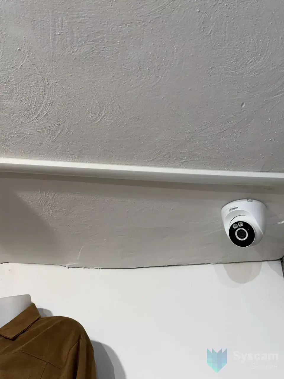 Caméra dôme compacte Dahua posée en hauteur dans un angle du magasin, au-dessus d'un portant de vêtements